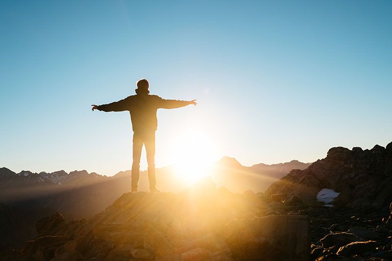 Happy man standing on a mountain with the sun rising in the background