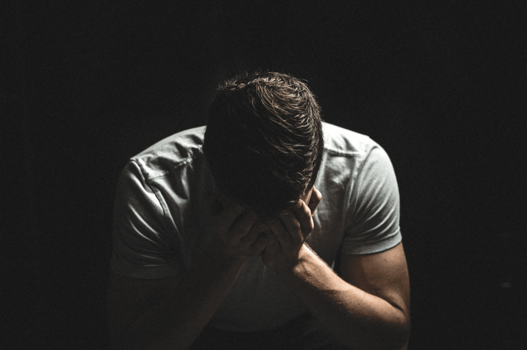 Man in a dark room with his head in hands, hunched over, symbolizing depression possibly related to synthetic opioid use.