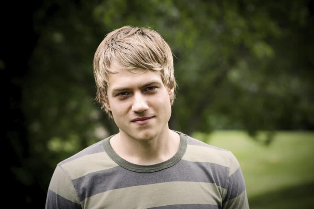 Blonde man staring at the camera with trees in the background