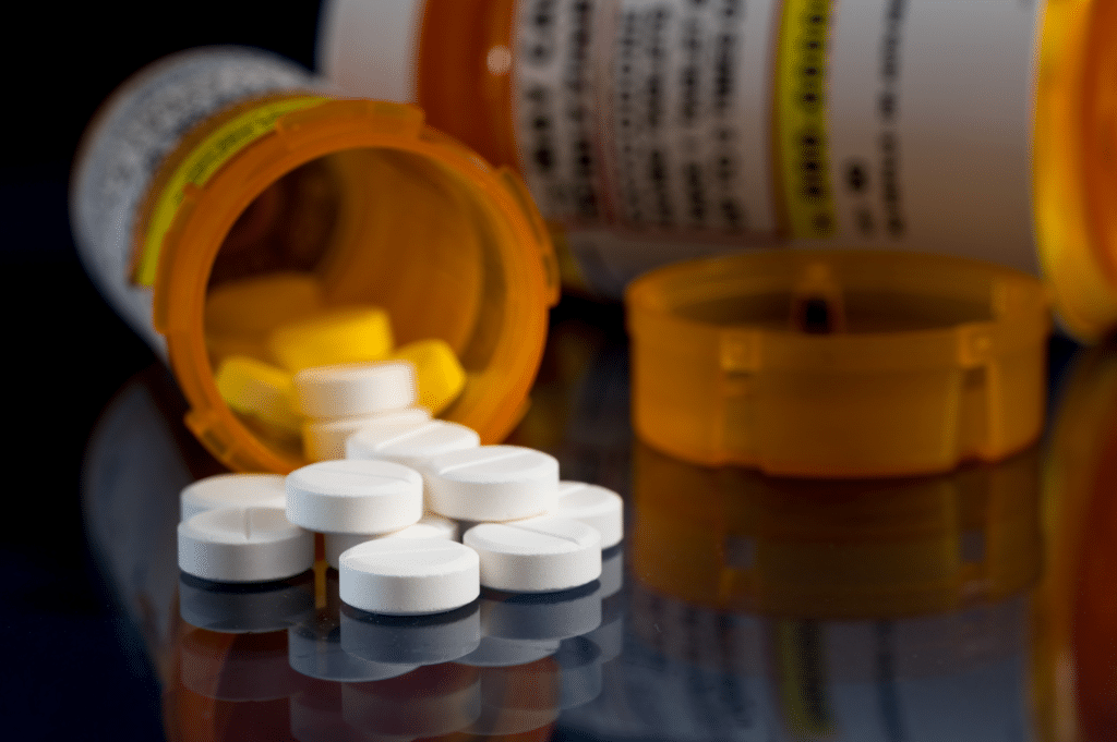 An open pill bottle with Oxycodone pills scattered across a table.