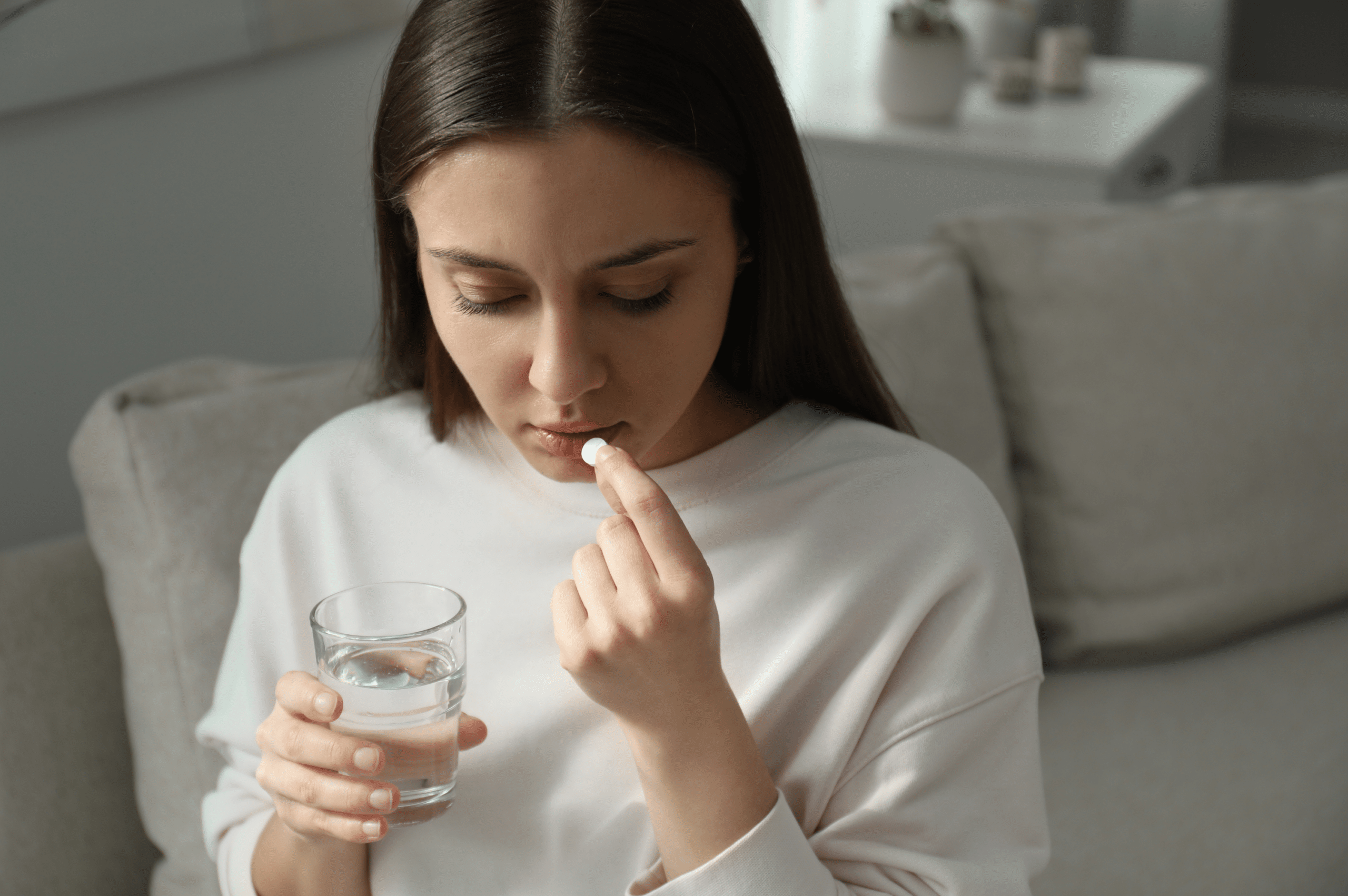 A woman holding a glass of water preparing to take an Oxycodone pill.