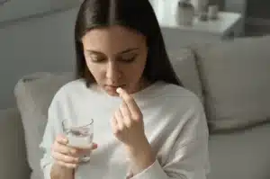 A woman holding a glass of water preparing to take an Oxycodone pill, depicting a moment of medication use and possible risk of Oxycodone addiction.